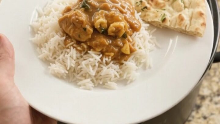 Slow cooker makhani chicken thighs in a glossy black pot, with rich orange-red sauce and butter pieces on top.