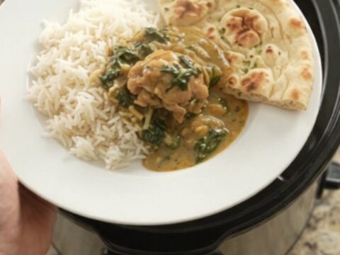 Slow cooker coconut spinach saag chicken thighs in a black crockpot, creamy green sauce with shredded chicken
