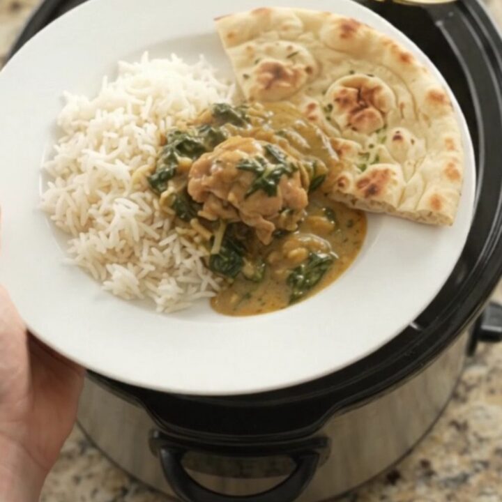 Slow cooker coconut spinach saag chicken thighs in a black crockpot, creamy green sauce with shredded chicken