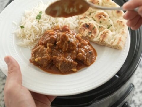 Slow cooker filled with bubbling garlic butter tikka masala lamb cubes