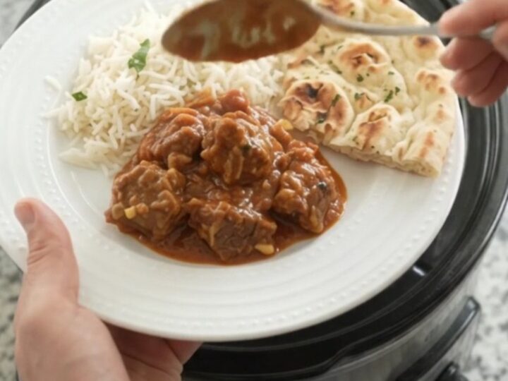 Slow cooker filled with bubbling garlic butter tikka masala lamb cubes