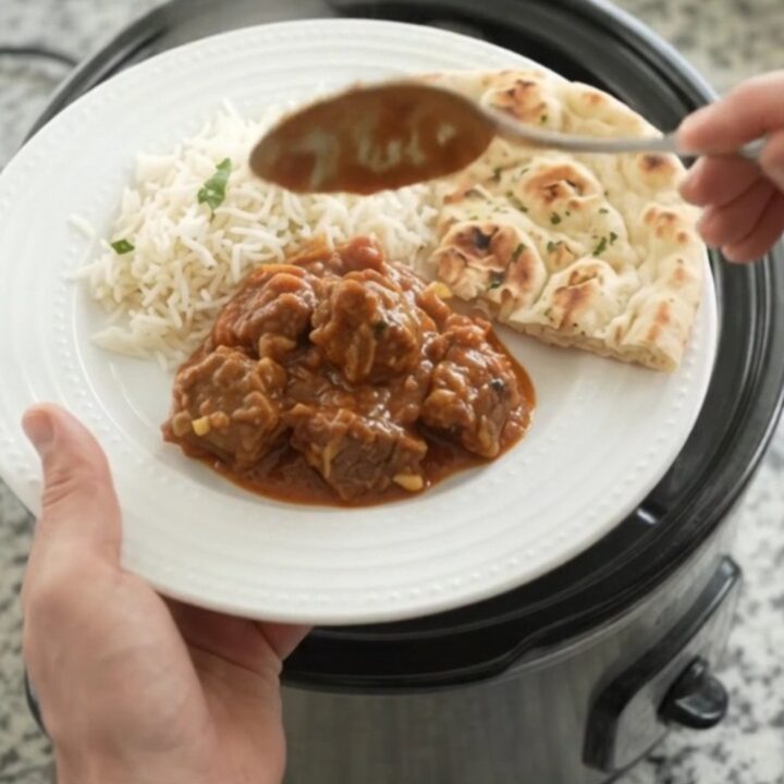 Slow cooker filled with bubbling garlic butter tikka masala lamb cubes