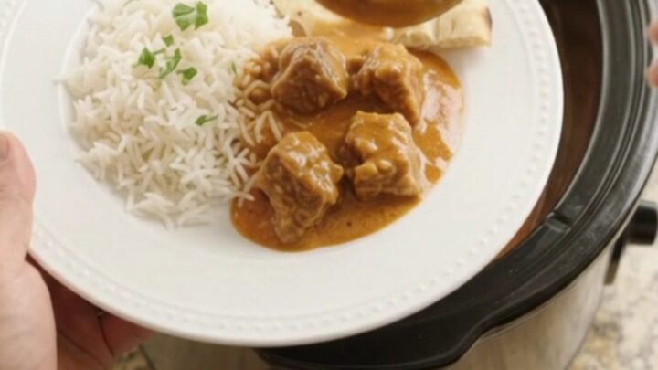 Tender lamb cubes in a rich orange-red coconut makhani sauce, garnished with fresh cilantro, in a slow cooker.
