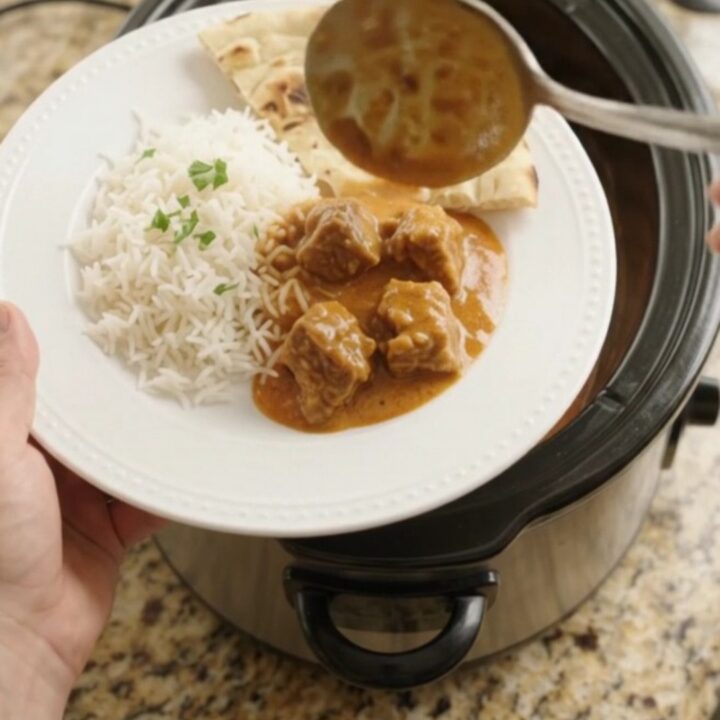 Tender lamb cubes in a rich orange-red coconut makhani sauce, garnished with fresh cilantro, in a slow cooker.