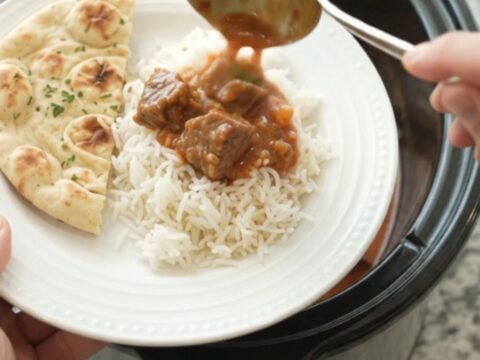 A slow cooker filled with coconut red curry lamb, with tender meat and peppers in a creamy sauce.