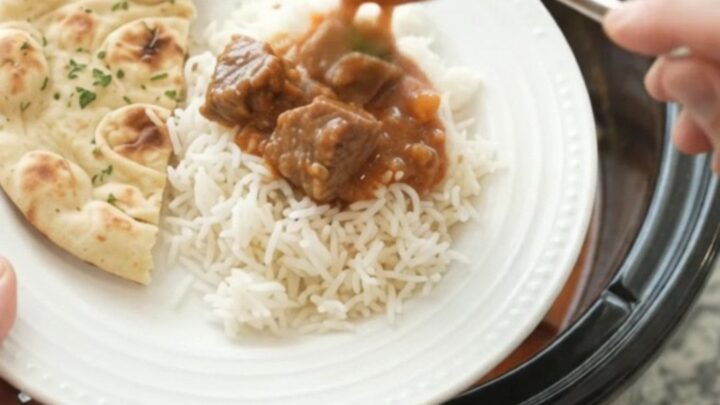 A slow cooker filled with coconut red curry lamb, with tender meat and peppers in a creamy sauce.