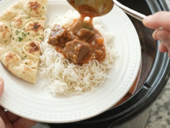 A slow cooker filled with coconut red curry lamb, with tender meat and peppers in a creamy sauce.