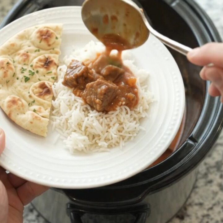A slow cooker filled with coconut red curry lamb, with tender meat and peppers in a creamy sauce.