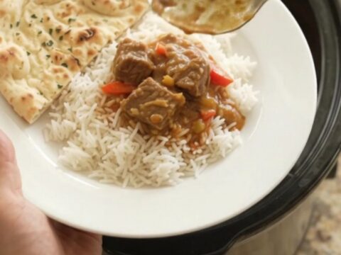 Creamy red curry lamb cubes in a slow cooker, garnished with fresh cilantro and served over rice.
