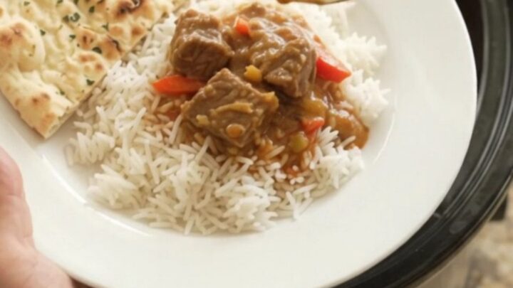 Creamy red curry lamb cubes in a slow cooker, garnished with fresh cilantro and served over rice.