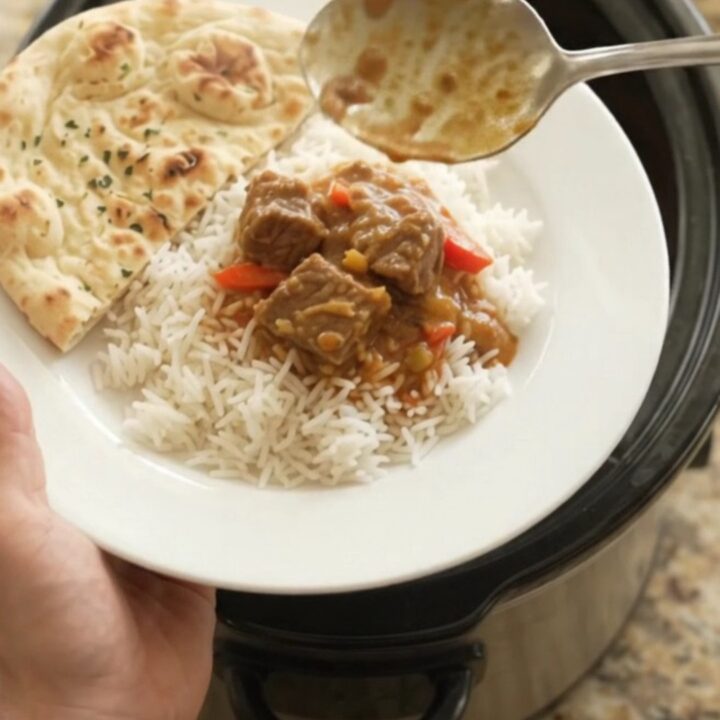 Creamy red curry lamb cubes in a slow cooker, garnished with fresh cilantro and served over rice.