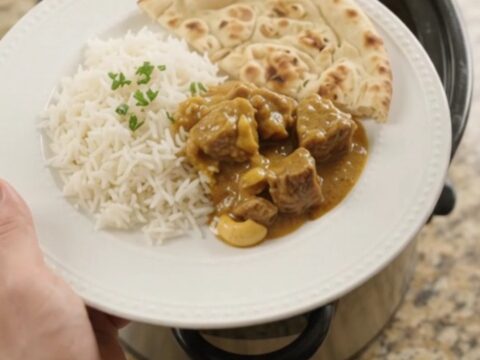 Slow cooker lamb korma in a black crockpot, garnished with fresh cilantro