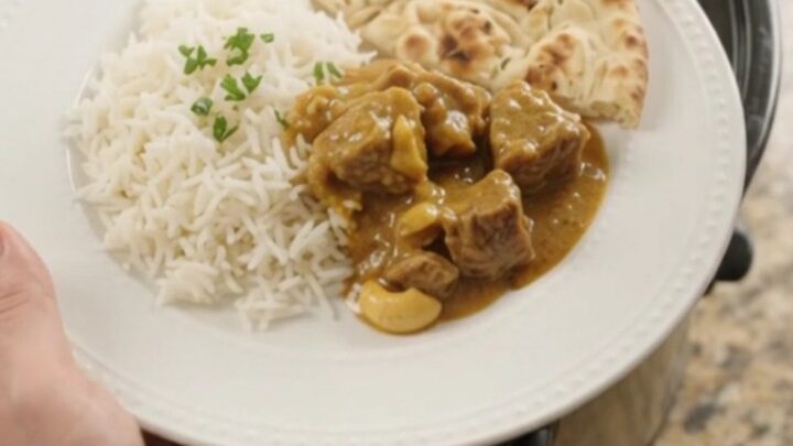 Slow cooker lamb korma in a black crockpot, garnished with fresh cilantro