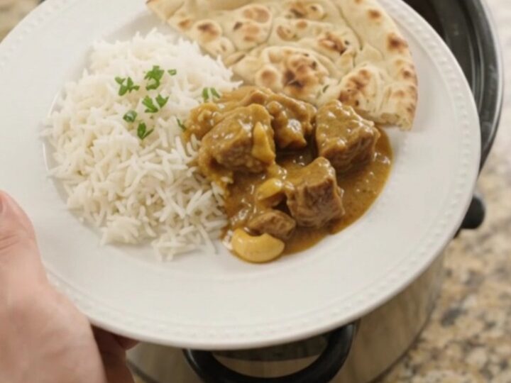 Slow cooker lamb korma in a black crockpot, garnished with fresh cilantro