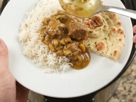 Slow cooker garlic butter golden korma lamb cubes in a black ceramic pot with sauce
