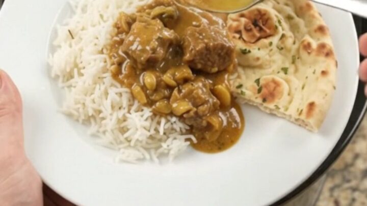 Slow cooker garlic butter golden korma lamb cubes in a black ceramic pot with sauce