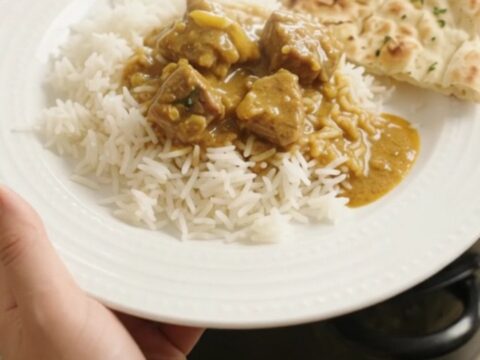 Slow cooker filled with golden coconut korma lamb curry, garnished with fresh cilantro leaves