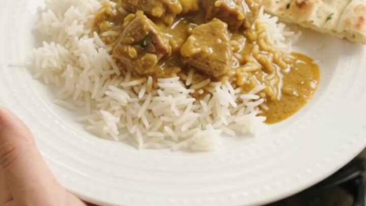 Slow cooker filled with golden coconut korma lamb curry, garnished with fresh cilantro leaves