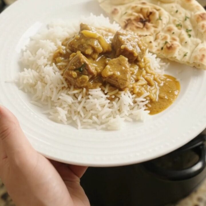 Slow cooker filled with golden coconut korma lamb curry, garnished with fresh cilantro leaves