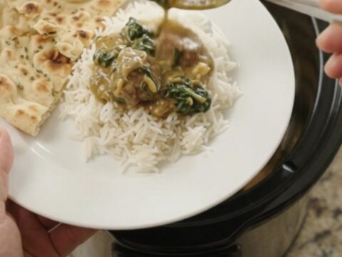 Slow cooker lamb saag with coconut cream, garnished with cilantro, in a black crockpot.