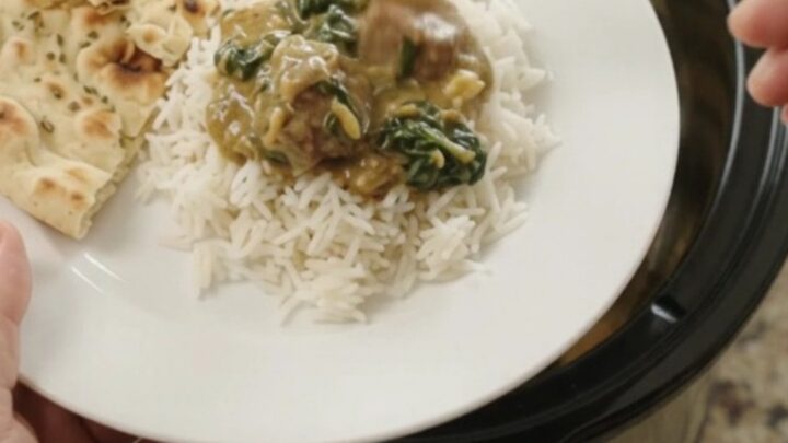 Slow cooker lamb saag with coconut cream, garnished with cilantro, in a black crockpot.