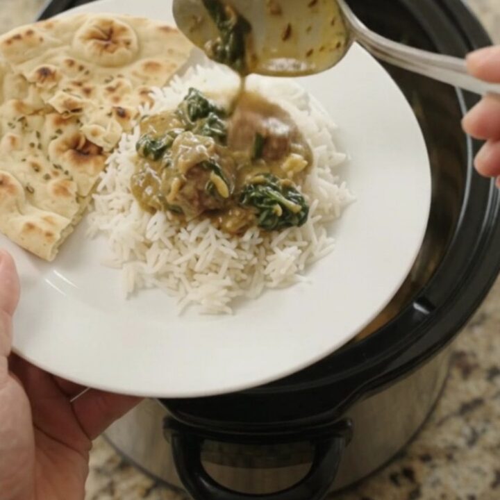 Slow cooker lamb saag with coconut cream, garnished with cilantro, in a black crockpot.