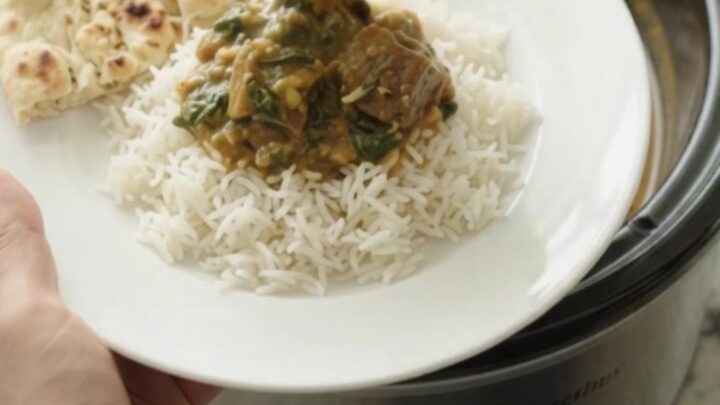 Slow cooker lamb saag in a black Crockpot, creamy emerald sauce with tender lamb cubes