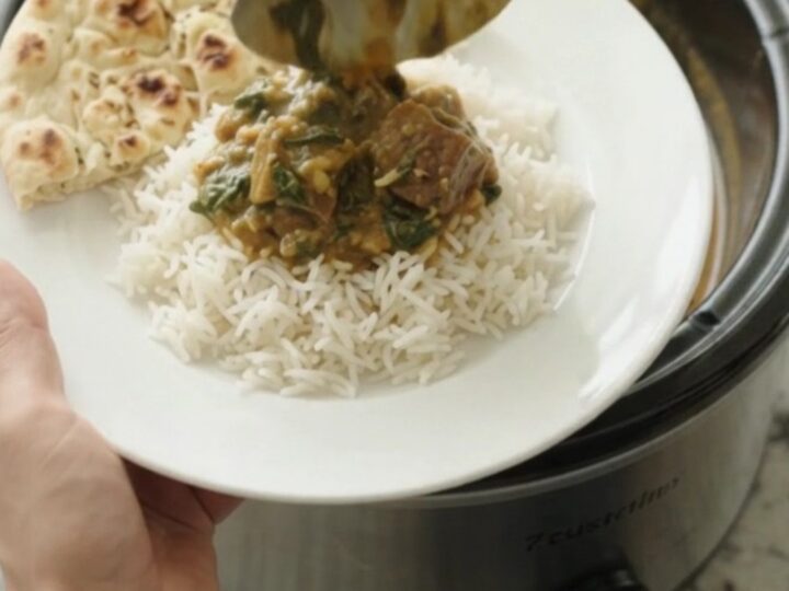 Slow cooker lamb saag in a black Crockpot, creamy emerald sauce with tender lamb cubes
