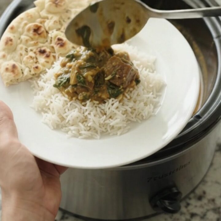 Slow cooker lamb saag in a black Crockpot, creamy emerald sauce with tender lamb cubes