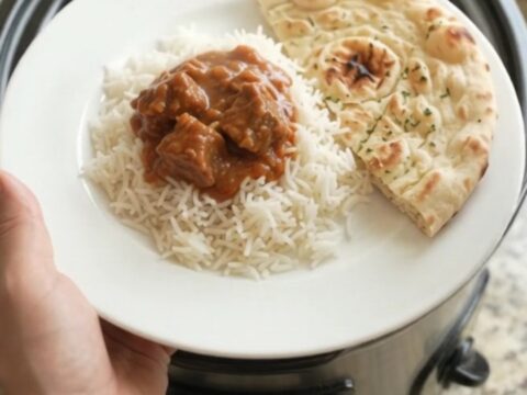 Slow cooker beef brisket tikka masala in a black crockpot, creamy crimson sauce with tender beef cubes