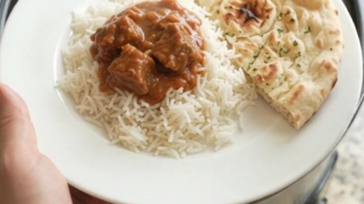 Slow cooker beef brisket tikka masala in a black crockpot, creamy crimson sauce with tender beef cubes