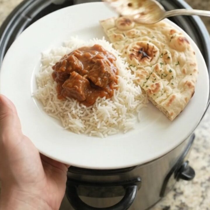 Slow cooker beef brisket tikka masala in a black crockpot, creamy crimson sauce with tender beef cubes