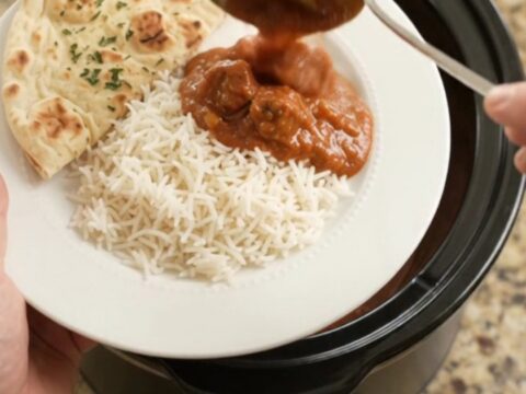 A slow cooker filled with tikka masala beef brisket, garnished with fresh cilantro and served with rice and naan.
