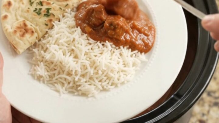 A slow cooker filled with tikka masala beef brisket, garnished with fresh cilantro and served with rice and naan.