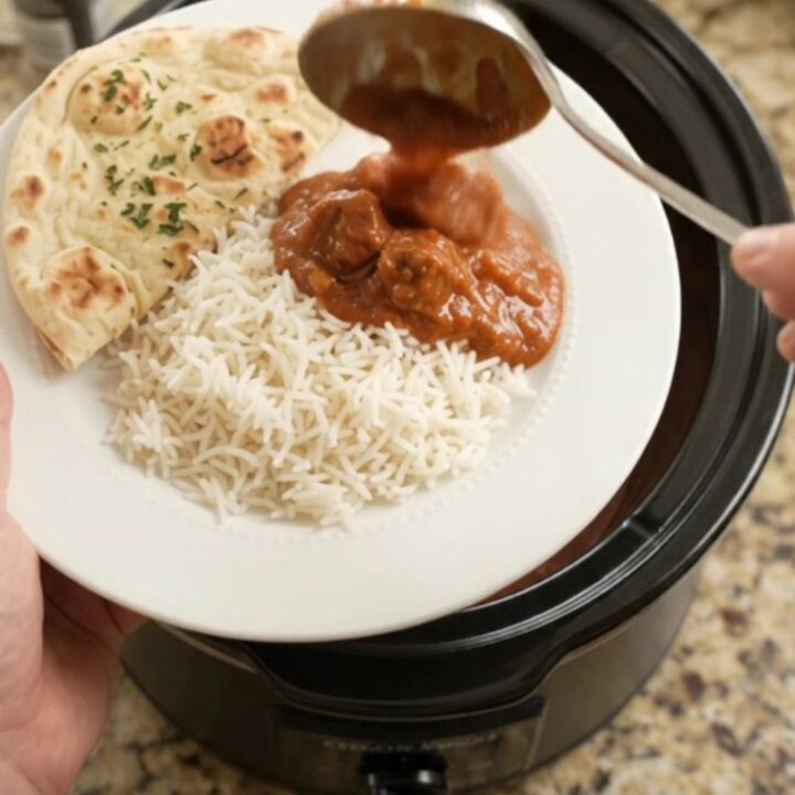 A slow cooker filled with tikka masala beef brisket, garnished with fresh cilantro and served with rice and naan.
