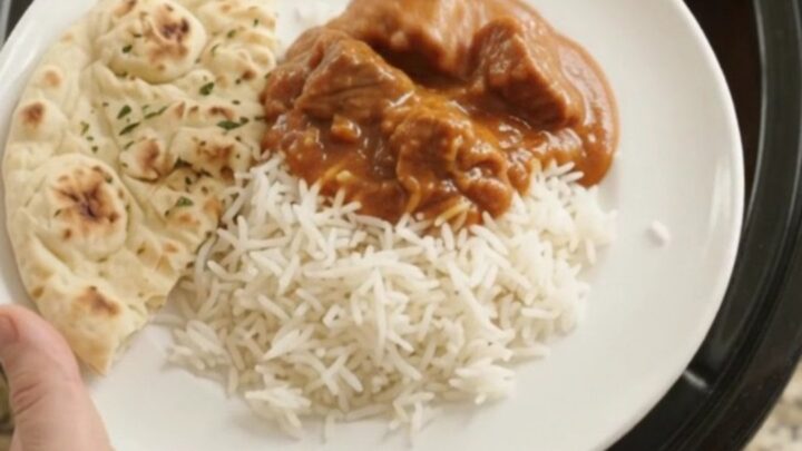 Slow cooker beef brisket tikka masala in a black ceramic pot, topped with cilantro