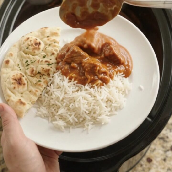 Slow cooker beef brisket tikka masala in a black ceramic pot, topped with cilantro