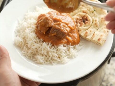 Slow cooker filled with creamy orange-red makhani beef brisket curry, garnished with butter
