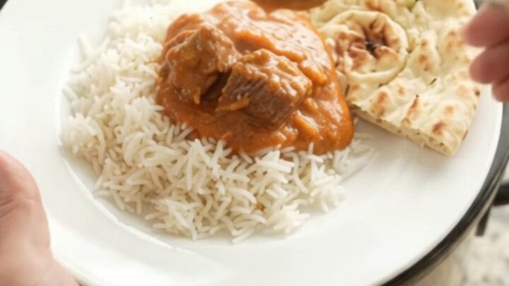 Slow cooker filled with creamy orange-red makhani beef brisket curry, garnished with butter