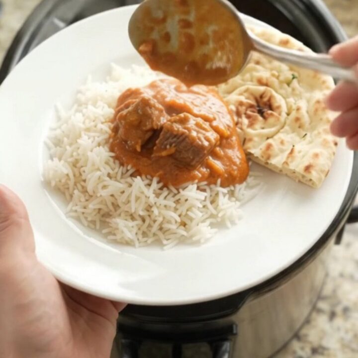 Slow cooker filled with creamy orange-red makhani beef brisket curry, garnished with butter