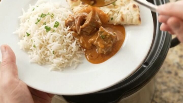 Slow-cooker beef brisket makhani masala in a black crockpot, creamy orange-red sauce with visible spices and cilantro.