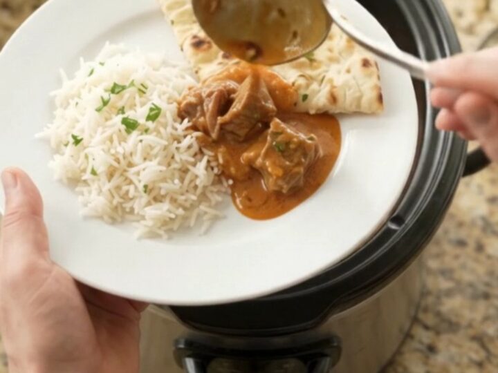 Slow-cooker beef brisket makhani masala in a black crockpot, creamy orange-red sauce with visible spices and cilantro.