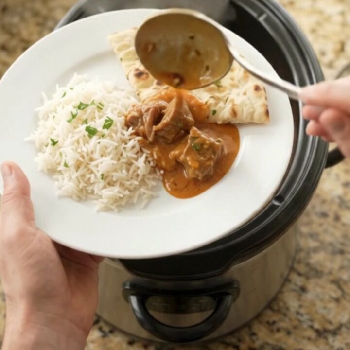 Slow-cooker beef brisket makhani masala in a black crockpot, creamy orange-red sauce with visible spices and cilantro.