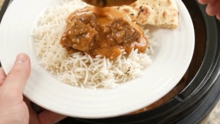 Slow cooker garlic butter makhani beef brisket in a black crockpot, topped with melted butter and yogurt