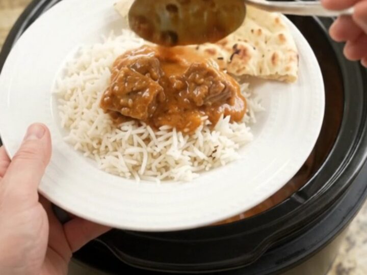 Slow cooker garlic butter makhani beef brisket in a black crockpot, topped with melted butter and yogurt