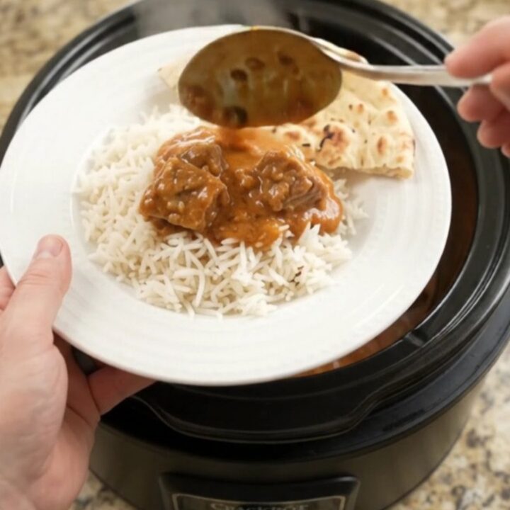 Slow cooker garlic butter makhani beef brisket in a black crockpot, topped with melted butter and yogurt