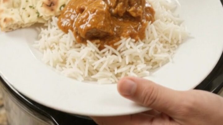 Slow cooker creamy ghee makhani masala beef brisket in a black ceramic crock, topped with cream