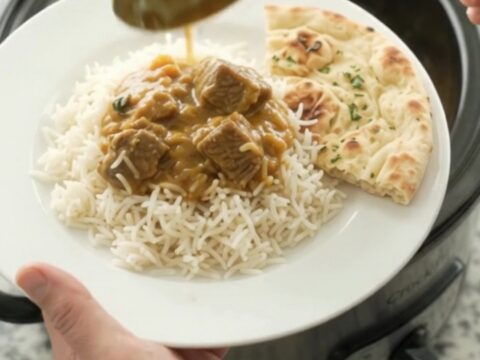Creamy golden korma beef brisket in a black slow cooker, topped with a swirl of cream and ghee, with steam rising.