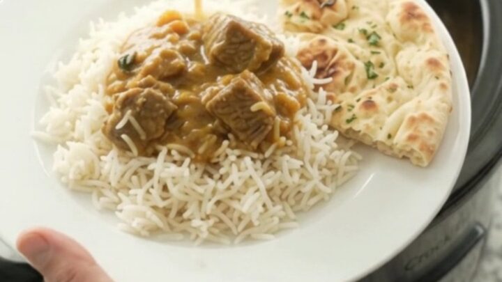 Creamy golden korma beef brisket in a black slow cooker, topped with a swirl of cream and ghee, with steam rising.