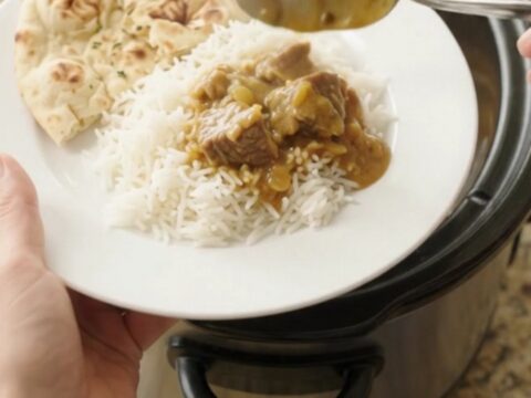 Golden korma beef brisket in a slow cooker, topped with cashew cream and butter pats.